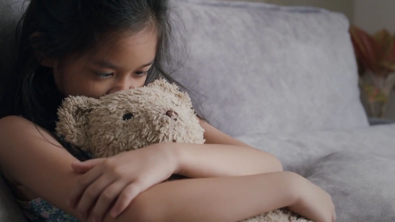 Live-action child holding teddy bear on couch