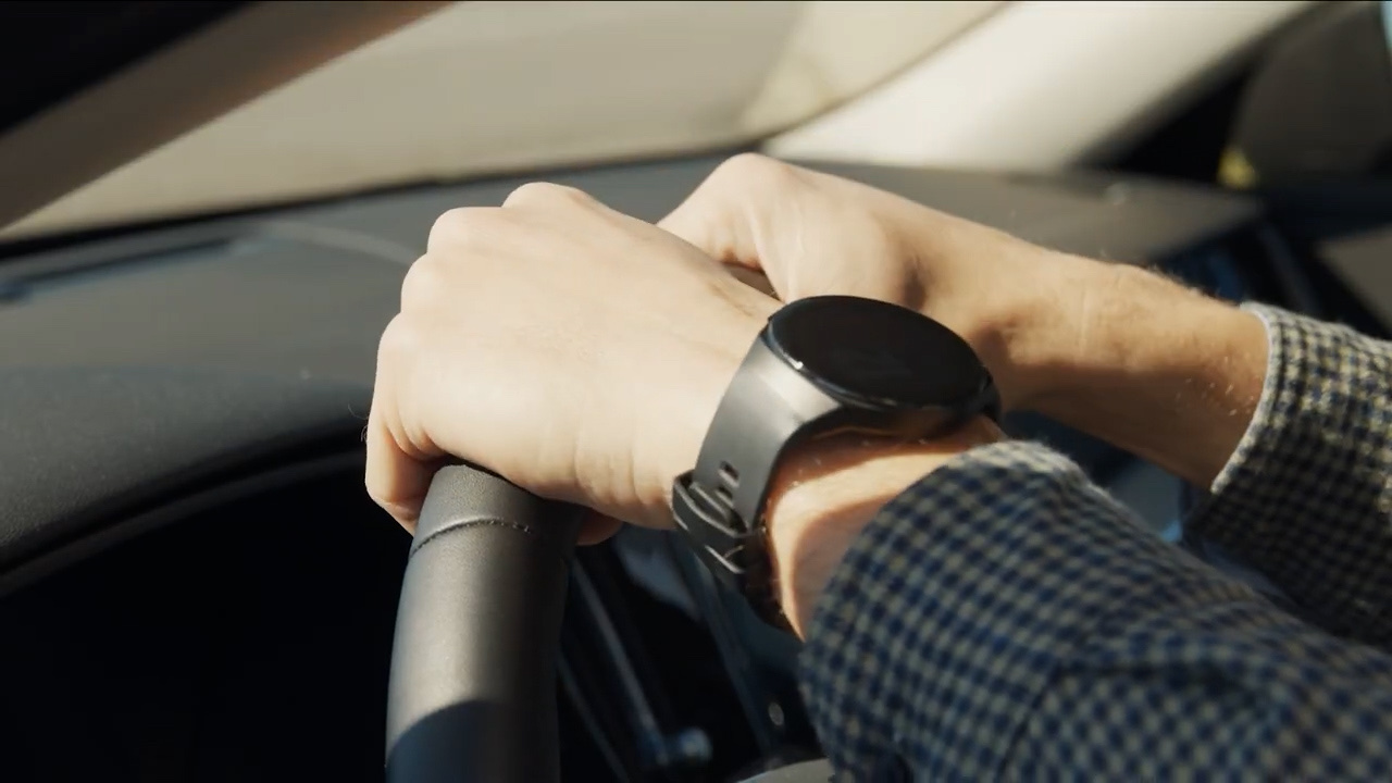 Live-action close-up of hands on car steering wheel with smartwatch driving down road